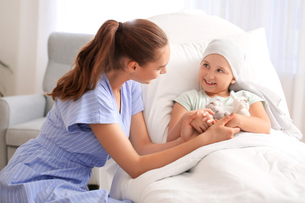 Mulher pegando nas mãos de criança com câncer deitada na cama