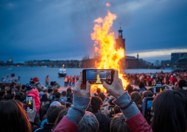 Pessoa, em multidão, registando pelo celular uma grande fogueira em celebração ao Walpurgis