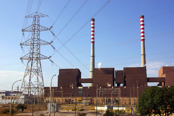 Vista de uma usina termoelétrica com uma torre de transmissão e grandes chaminés.