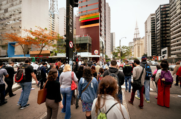 Dezenas de pessoas esperando para atravessar em uma faixa de pedestres na Avenida Paulista, em São Paulo, no Brasil.