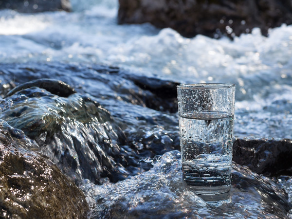 Copo de vidro com água sobre uma pedra em um região com curso d’água.
