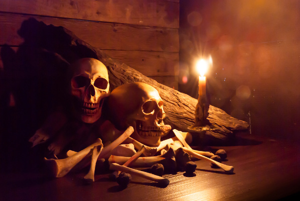 Caveiras e ossos em ambiente escuro iluminado com vela, comum em decoração de Halloween.