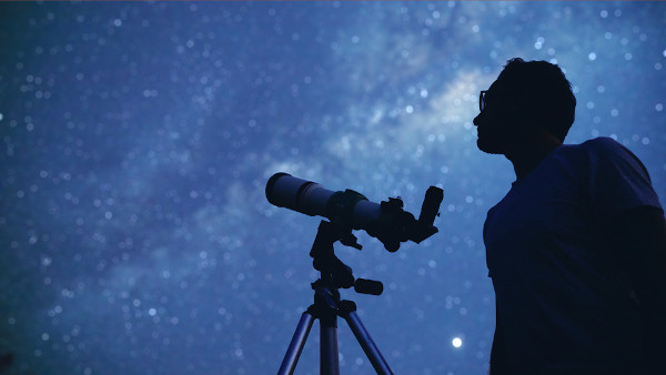 Homem diante de telescópio para observar o céu noturno