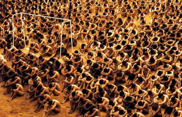 Cena do filme Carandiru com centenas de detentos nus e sentados em campo de futebol.