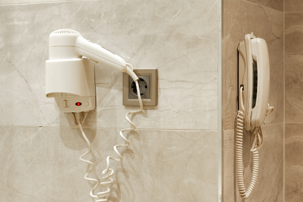 Secador de cabelo e telefone dispostos na parede de um hotel como representação da potência elétrica.