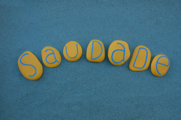 Sete pequenas pedras amarelas agrupadas formando o escrito “saudade” em alusão ao Dia da Saudade, celebrado em 30 de janeiro.