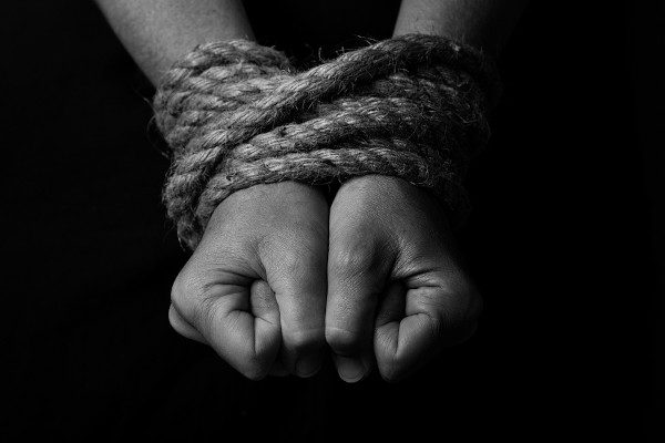 Mãos amarradas por uma corda representando a ideia de trabalho escravo no Brasil atual, violação grave dos direitos humanos.