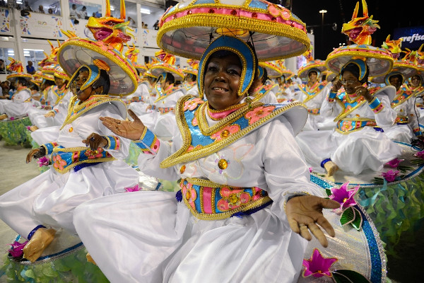 Mulheres durante o desfile de uma escola de samba, com fantasias de Carnaval coloridas e bem elaboradas.