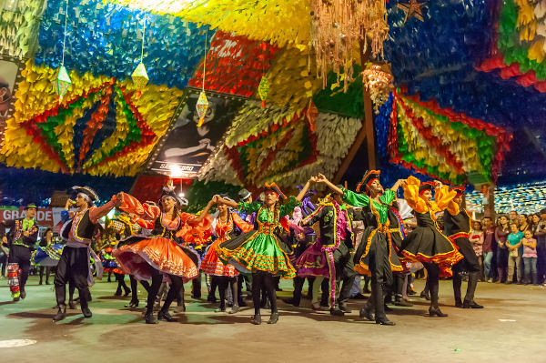 Mulheres e homens, com roupas coloridas, dançando quadrilha em um salão na cidade de Campina Grande, na Paraíba.