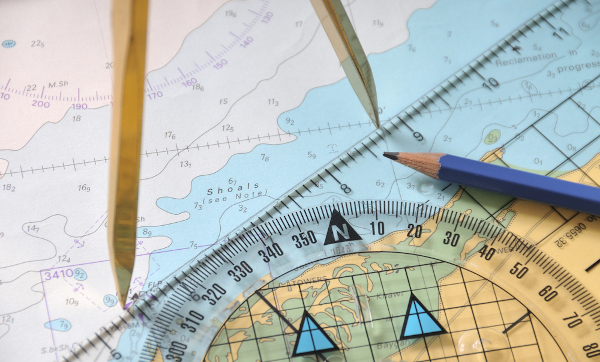 Compasso, régua, transferidor e lápis sobre mapa, em alusão ao conceito de escala cartográfica.