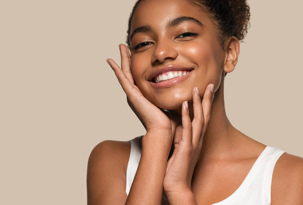 Mulher jovem de pele negra sorrindo com as mãos no rosto; a pele faz parte do sistema tegumentar.