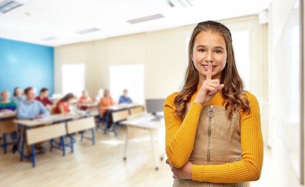 Garota em sala de aula faz o gesto do pedido de silêncio com a mão.