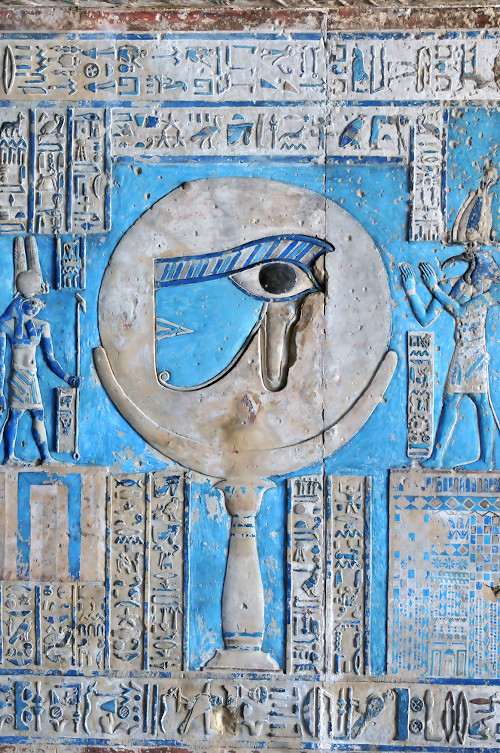 Olho de Hórus esculpido na parede de um templo egípcio, entre hieróglifos e dois deuses.