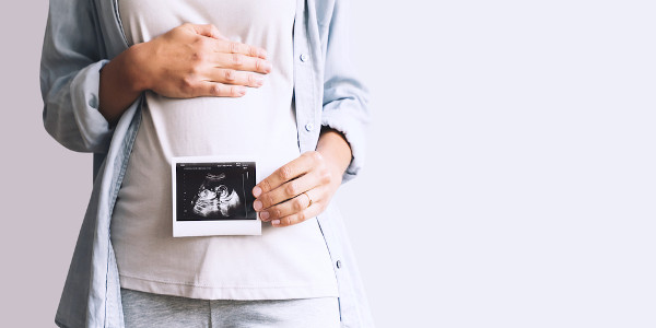 Mulher grávida mostra ultrassom do bebê que está gestando.