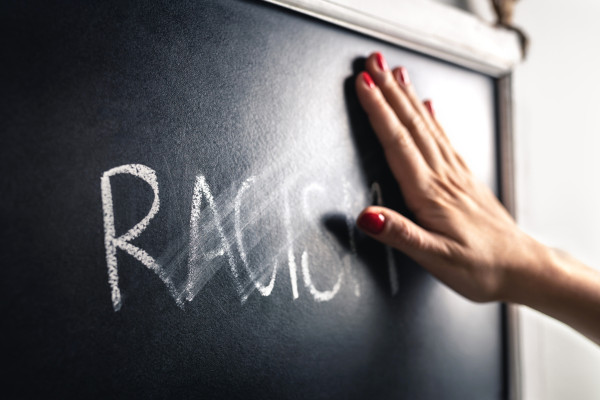 Mão apaga a palavra racismo escrita em quadro-negro