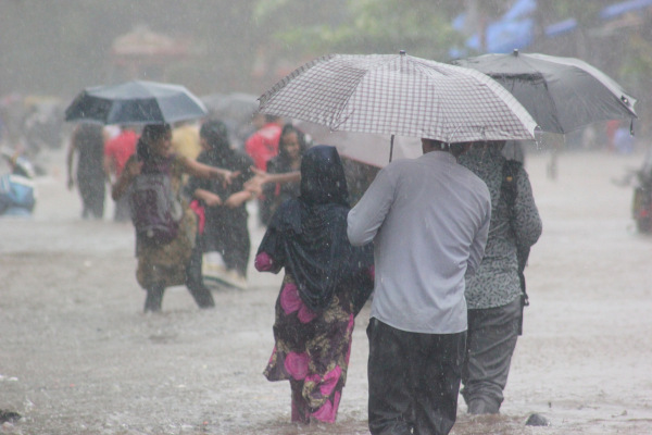 Pessoas com guarda-chuvas e chuva intensa ocorrendo em decorrência das monções.
