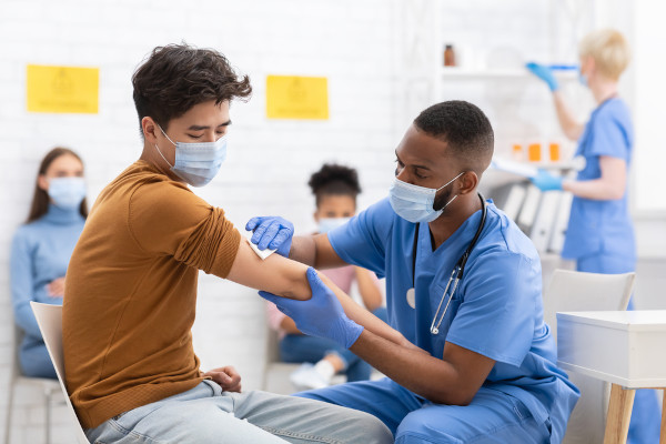 Enfermeiro limpando braço de paciente para aplicação de vacina, ambos de máscaras.