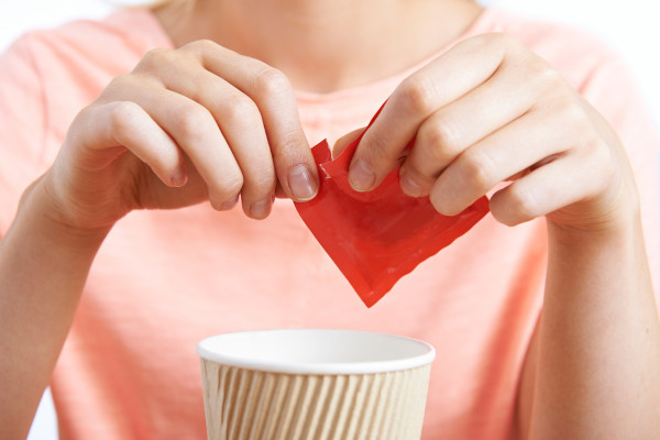Mulher colocando adoçante artificial à base de aspartame em um copo de café.