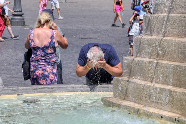 Homem molhando o rosto em uma fonte, em texto sobre domo de calor. 