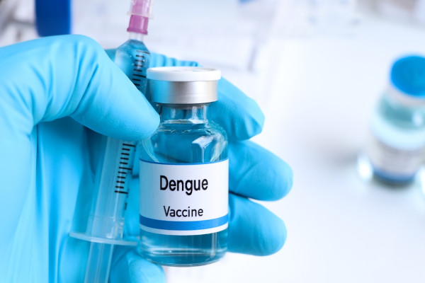 Imagem aproximada da mão de um enfermeiro segurando um frasco contendo a vacina da dengue.