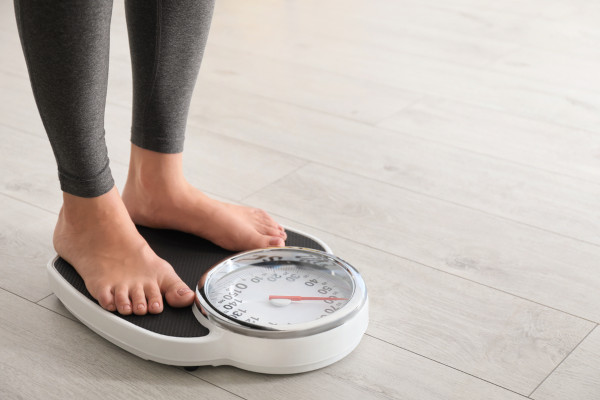 Mulher medindo sua massa (e não o seu peso) em uma balança.