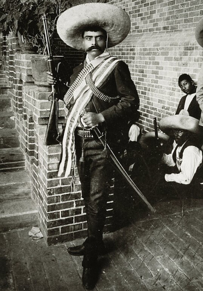 Fotografia em preto e branco de Emiliano Zapata segurando uma espada e uma arma de fogo.