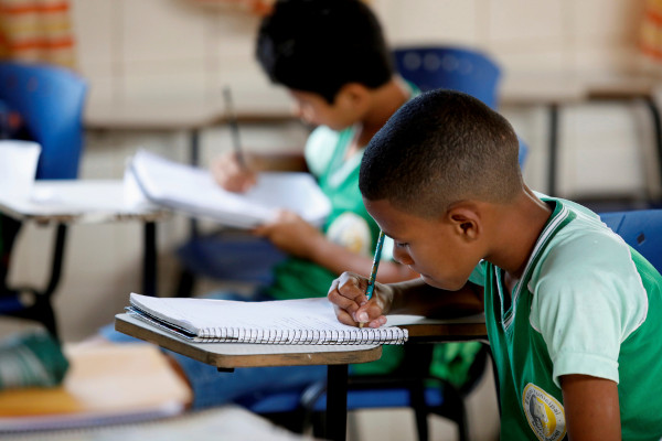 Menino escrevendo em caderno, em texto sobre educação no Brasil
