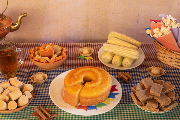 Mesa com diversas comidas típicas da Festa Junina dispostas sobre uma toalha xadrez.