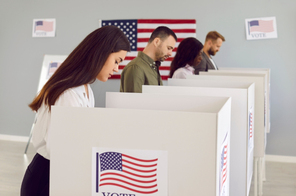 Jovens votando em cabine com bandeira estadunidense, uma alusão às eleições nos Estados Unidos.