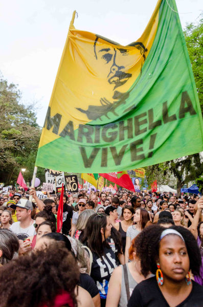 Pessoas em protesto segurando faixa com imagem de Carlos Marighella.