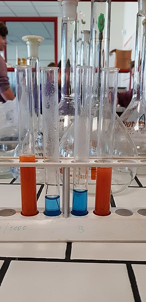 Vidros de laboratório com solução laranja e azul, para teste de Fehling, com aldeídos e cetonas.