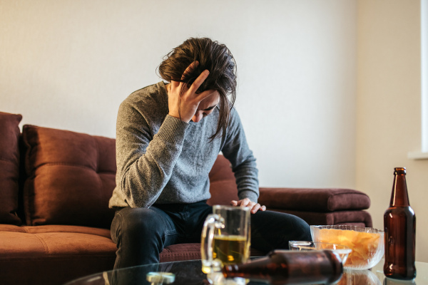 Homem coloca mão na cabeça diante de várias bebidas, em referência ao alcoolismo. Homem coloca mão na cabeça diante de várias bebidas, em referência ao alcoolismo.