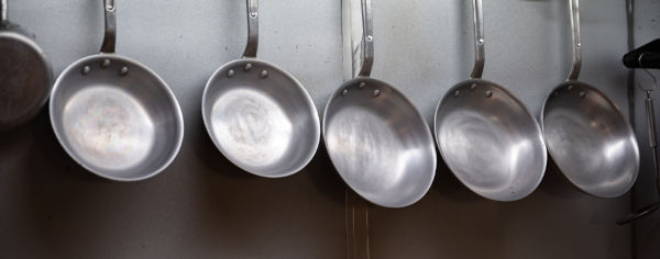 Panelas de aço inoxidável penduradas em suporte, o material é exemplo de solução sólida.