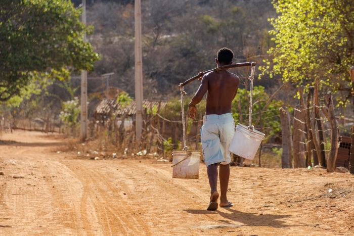 Homem carregando baldes em região seca do Nordeste, área afetada pela indústria da seca.