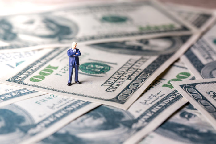 Figura de um homem em cima de notas de dólares, em alusão aos super-ricos.
