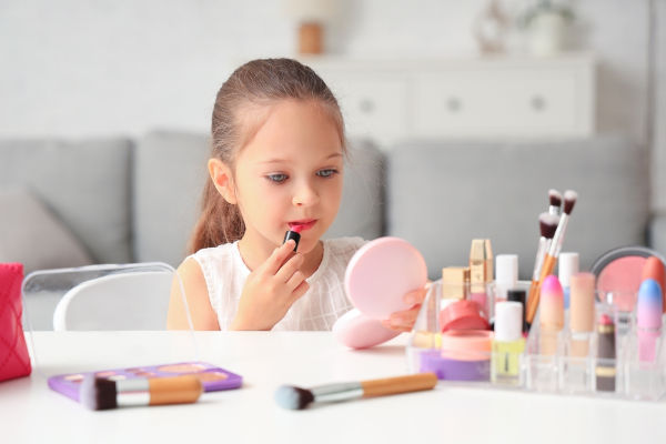 Menina se maquiando diante de um espelho, em alusão à adultização infantil.