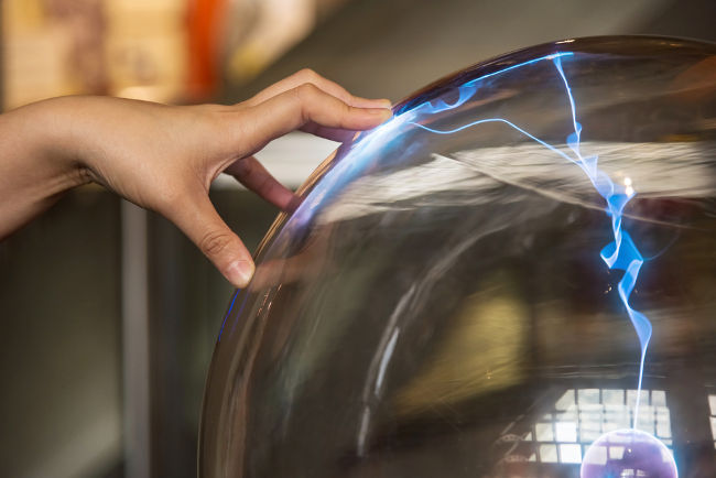 Os gases ionizados dentro da cúpula do globo de plasma emitem luz visível quando acelerados pelo eletrodo central.