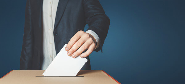Mão de homem depositando voto em urna, em alusão à democracia.