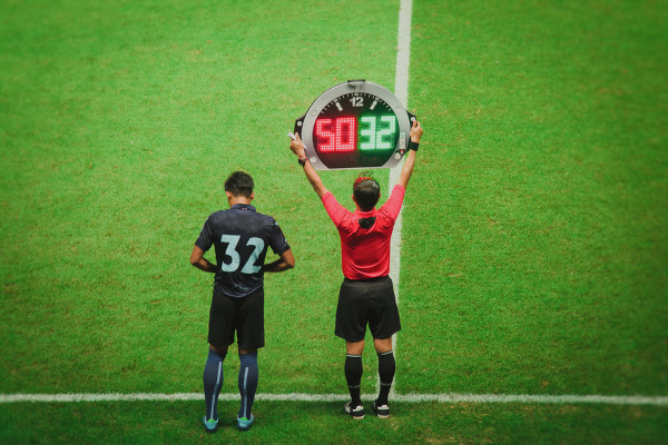 Homem levantando painel eletrônico de substituição de um jogador de futebol, uma invenção brasileira.