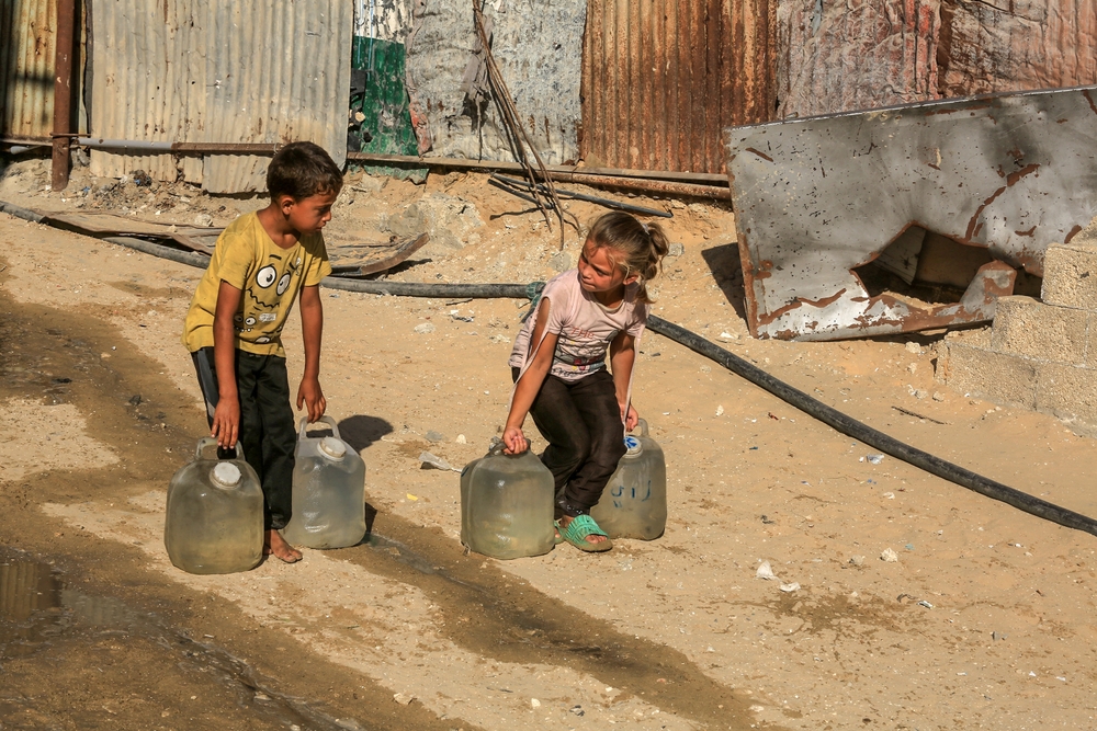 duas crianças palestinas carregando galão de água